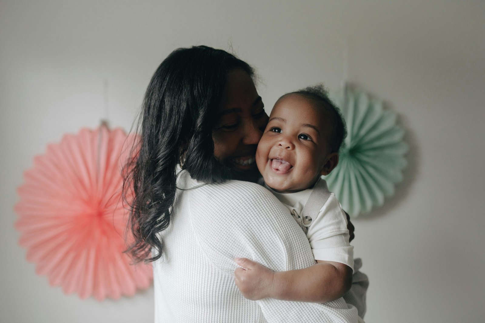 A mother joyfully holds her smiling baby, showcasing warmth and affection indoors.